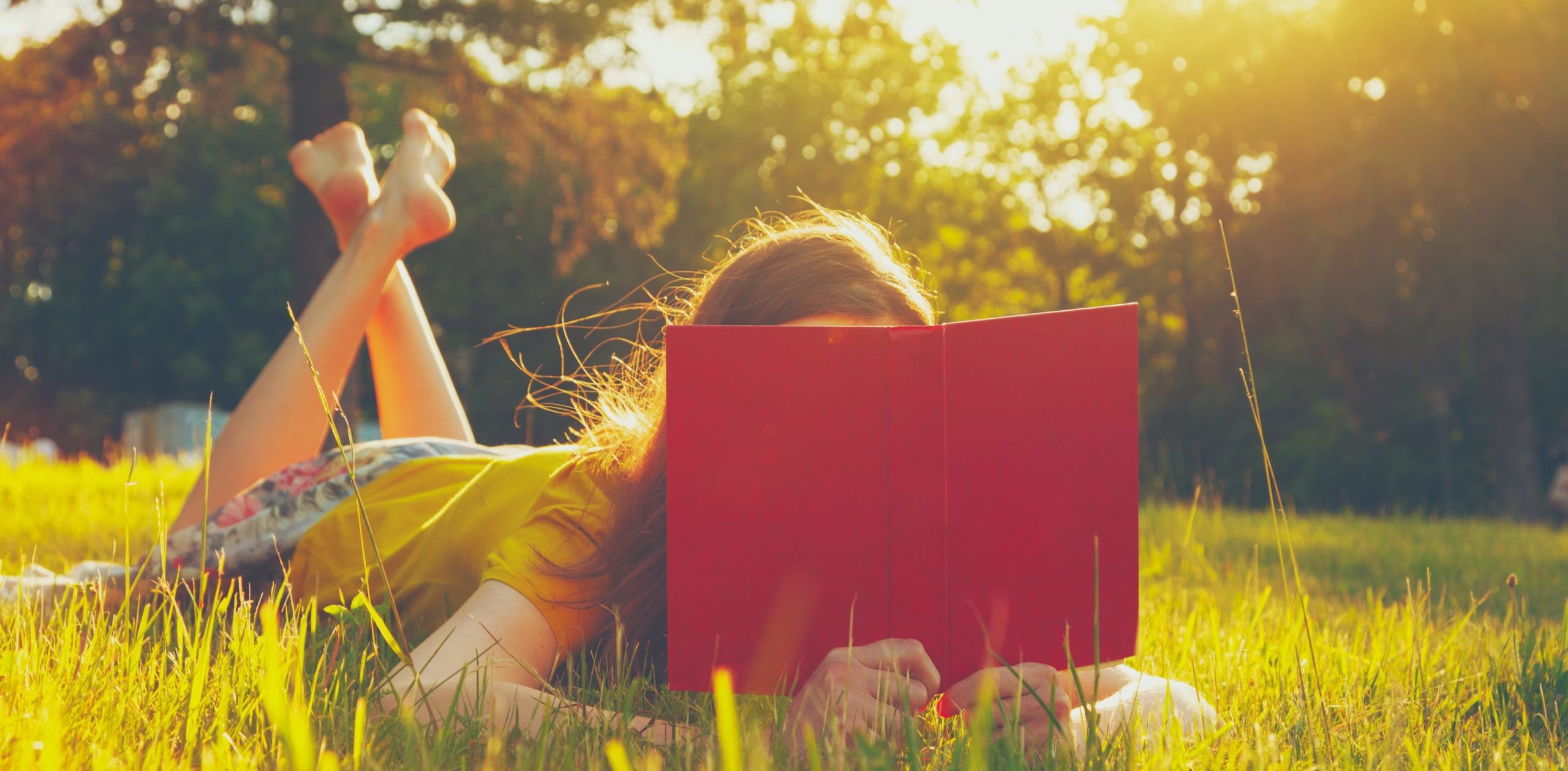 girl laying on grass reading a book
